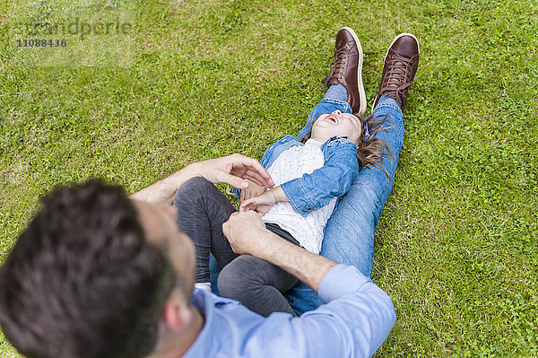 Vater kitzelt Tochter auf der Wiese im Park