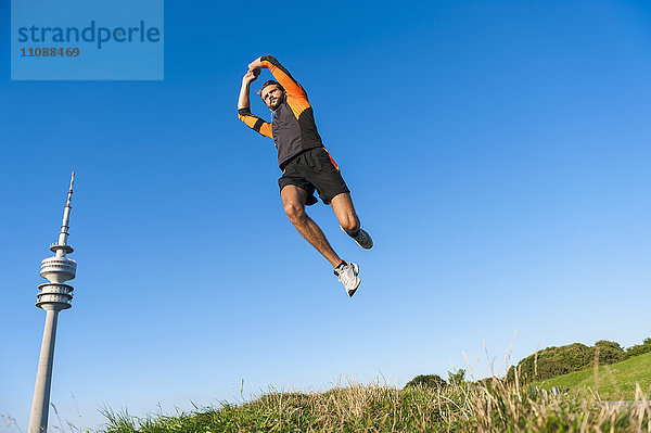 Sportler beim Springen auf der Wiese unter blauem Himmel