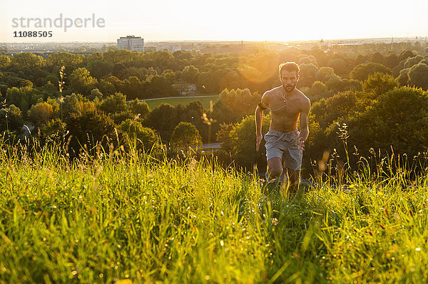Barechested Mann läuft auf Wiese im Park bei Sonnenuntergang
