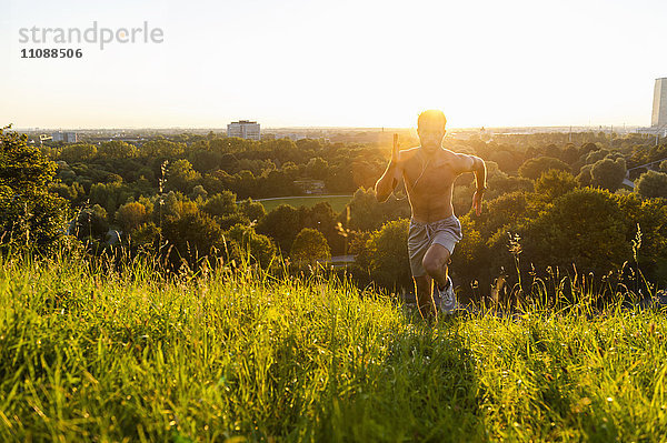 Barechested Mann läuft auf Wiese im Park bei Sonnenuntergang