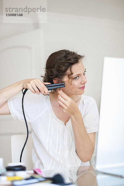 Frau zu Hause  die ihr Haar mit einem Haarglätter macht.