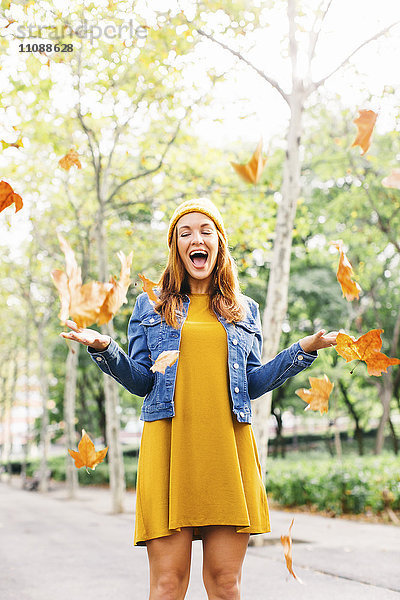 Fröhliche junge Frau wirft Herbstlaub in die Luft