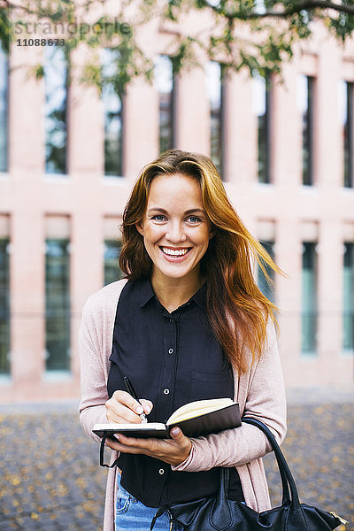 Porträt einer lächelnden jungen Frau mit Notizbuch