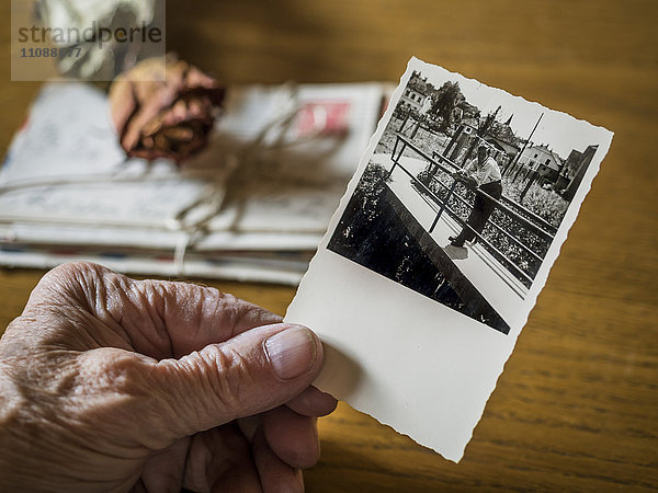 Alte Frau hält Bild ihrer Jugendfreundin in der Hand  alte Briefe und getrocknete Rose