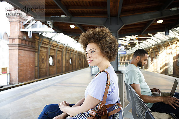 Junge Frau sitzt auf der Bank am Bahnhof