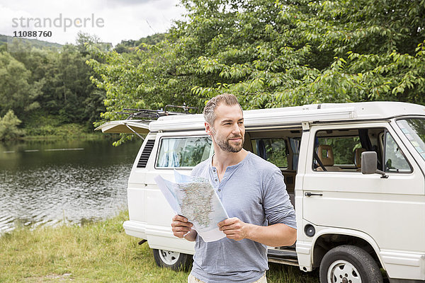 Mann mit Karte an einem Van am Seeufer