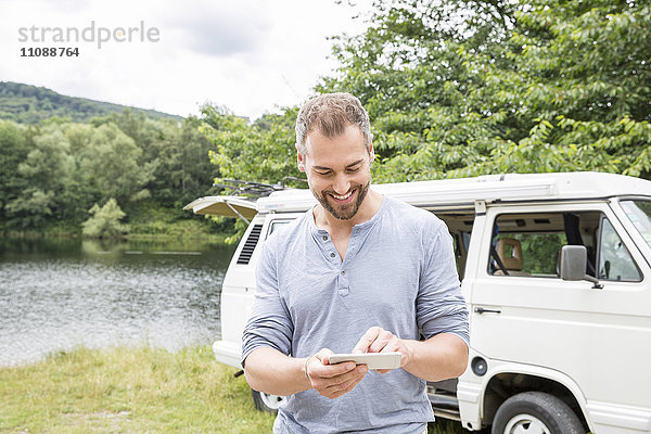 Lächelnder Mann mit Handy in einem Van am Seeufer
