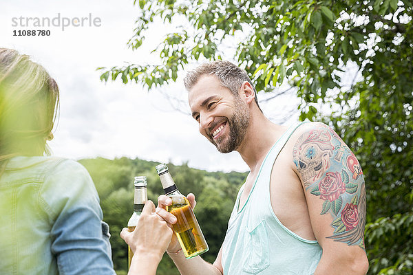 Lächelndes Paar klirrende Bierflaschen in der Natur