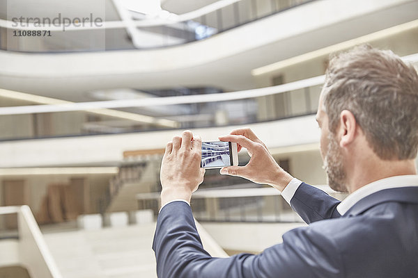 Geschäftsmann macht Handyfoto im modernen Bürogebäude