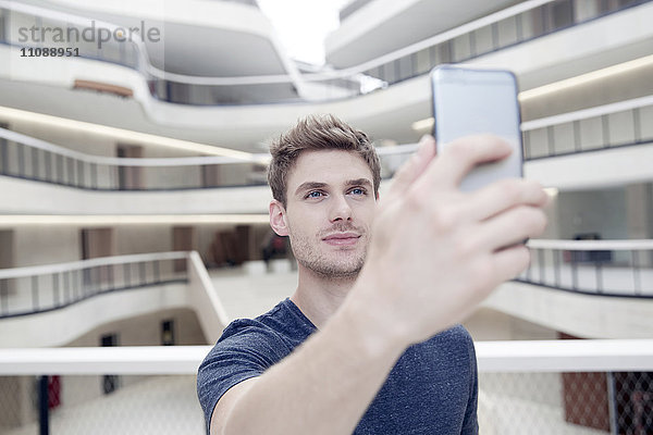 Junger Mann  der einen Selfie in einem modernen Bürogebäude nimmt.