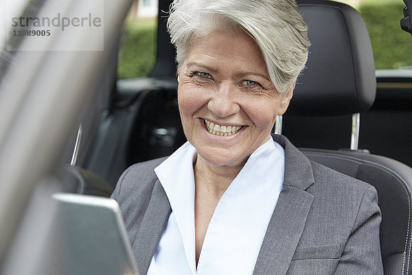 Porträt einer lächelnden Geschäftsfrau mit Tablette im Auto sitzend