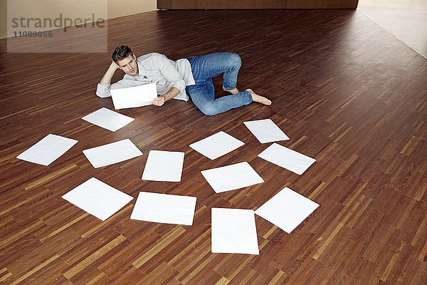 Junger Mann liegt auf dem Boden und schaut auf ein Blatt Papier.