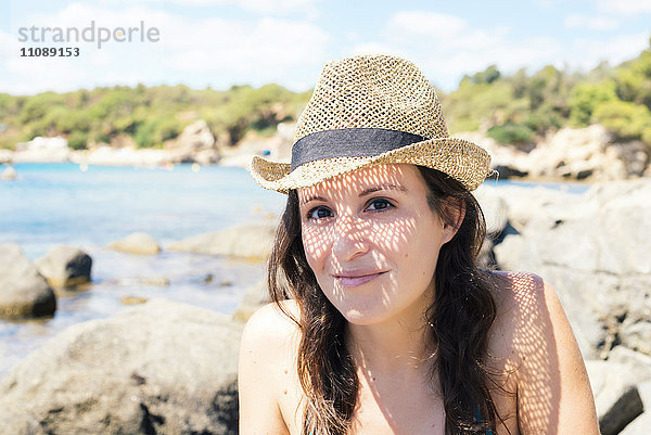Porträt einer lächelnden Frau mit Strohhut am Strand