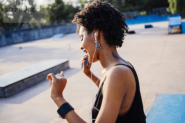 Lächelnde junge Frau mit Kopfhörern tanzend im Skatepark