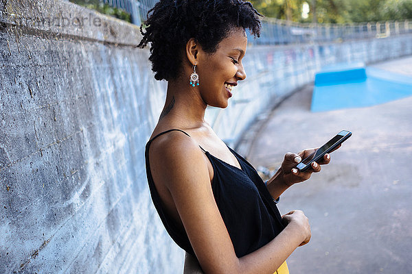 Lächelnde junge Frau im Skatepark mit Blick auf das Handy
