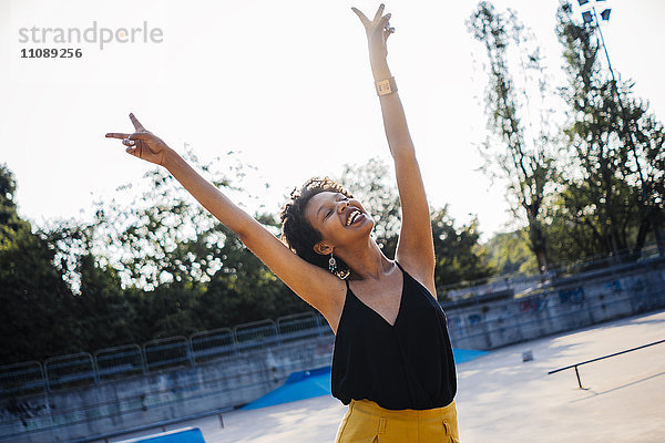 Glückliche junge Frau im Skatepark mit Siegeszeichen