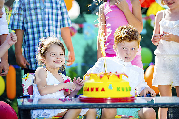 Kleines Mädchen und kleiner Junge feiern Geburtstag im Garten mit Freunden und Familie