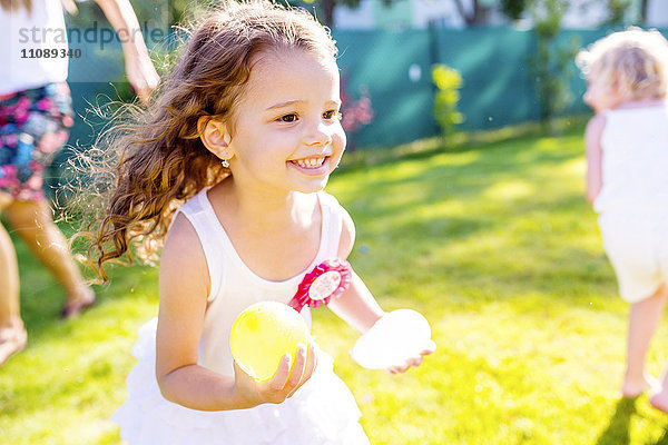 Kleines Mädchen beim Spaß mit Wasserbomben im Garten