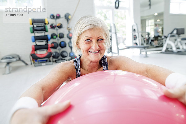 Porträt einer lächelnden reifen Frau mit Fitnessball in der Turnhalle