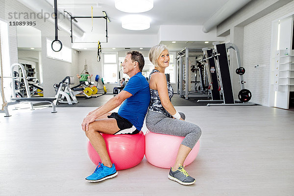 Senior-Mann und reife Frau sitzen auf Fitnessbällen in der Turnhalle
