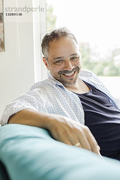 Porträt eines lächelnden Mannes  der zu Hause auf der Couch sitzt.