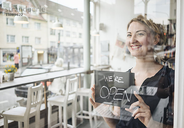 Lächelnde Frau in einem Café mit offenem Schild an der Glasscheibe