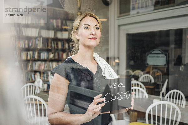 Frau in einem Café  die ein geschlossenes Schild an der Glasscheibe befestigt.