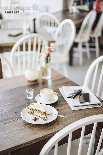 Handy  Sonnenbrille  Kuchen und Tasse Kaffee auf dem Tisch im Cafe