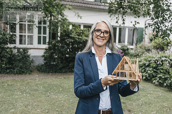 Lächelnde Geschäftsfrau mit Architekturmodell im Garten