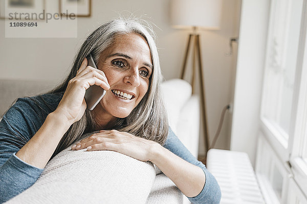 Lächelnde Frau sitzt auf der Couch und telefoniert mit dem Handy.