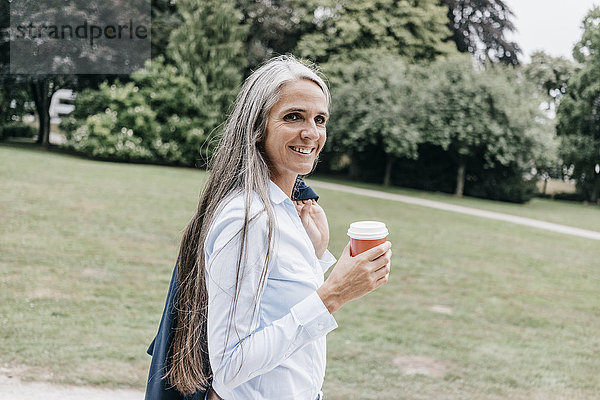 Lächelnde Frau mit Kaffee zum Mitnehmen im Park
