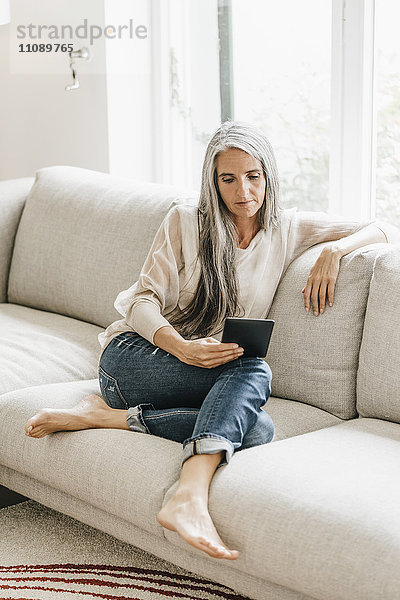Frau mit langen grauen Haaren sitzt auf der Couch mit E-Book