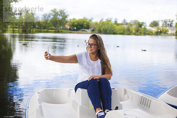 Russland  Tichwin  Teenagermädchen mit Smartphone  im Boot sitzend  Selfie