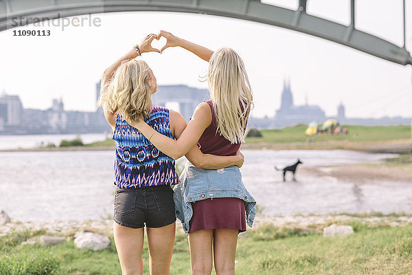 Zwei beste Freunde  die das Herz mit den Händen am Flussufer formen.