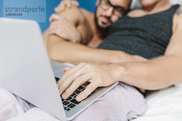 Schwules Paar im Bett liegend  mit Laptop