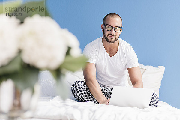 Homosexuell Mann sitzt auf dem Bett  mit Laptop