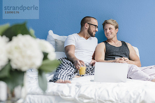 Schwules Paar im Bett liegend  mit Laptop