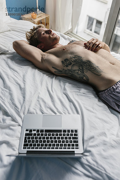Schwuler Mann mit Tattoo auf dem Bett liegend