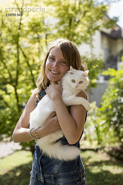 Glückliche Frau mit Katze auf den Armen im Garten
