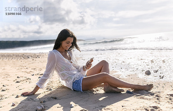Spanien  Asturien  schöne junge Frau mit Smartphone am Strand