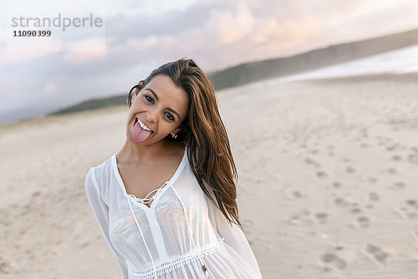 Porträt einer jungen Frau am Strand  herausstehende Zunge