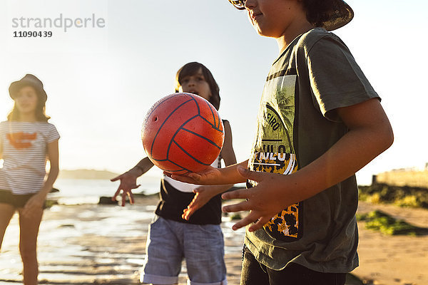 Kinder spielen mit einem Ball am Strand bei Sonnenuntergang