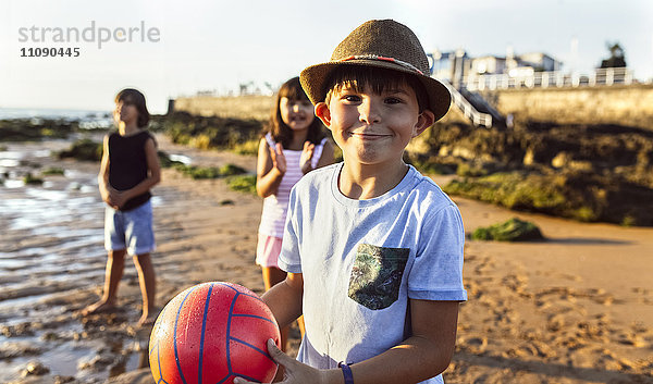 Portrait eines Jungen mit einem Ball am Strand bei Sonnenuntergang