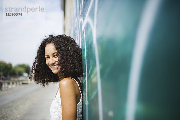 Porträt einer lächelnden jungen Frau  die sich an die Wand lehnt.
