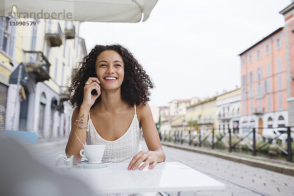 Porträt einer lächelnden jungen Frau am Telefon im Straßencafé