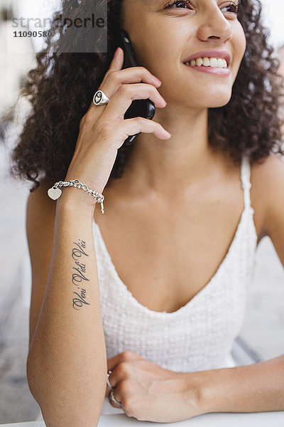 Lächelnde junge Frau mit Tattoo auf dem Unterarm am Telefon