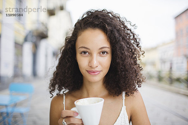 Porträt einer jungen Frau beim Kaffeetrinken im Straßencafé