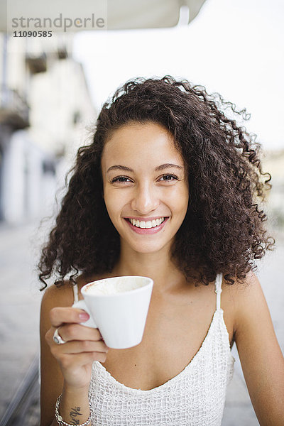 Porträt einer glücklichen jungen Frau beim Kaffeetrinken im Straßencafé