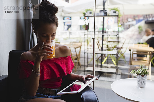 Junge Frau trinkt ein Glas Orangensaft in einem Coffee-Shop und schaut sich die Tablette an.