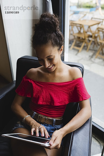 Lächelnde junge Frau sitzend in einem Café mit Tablette